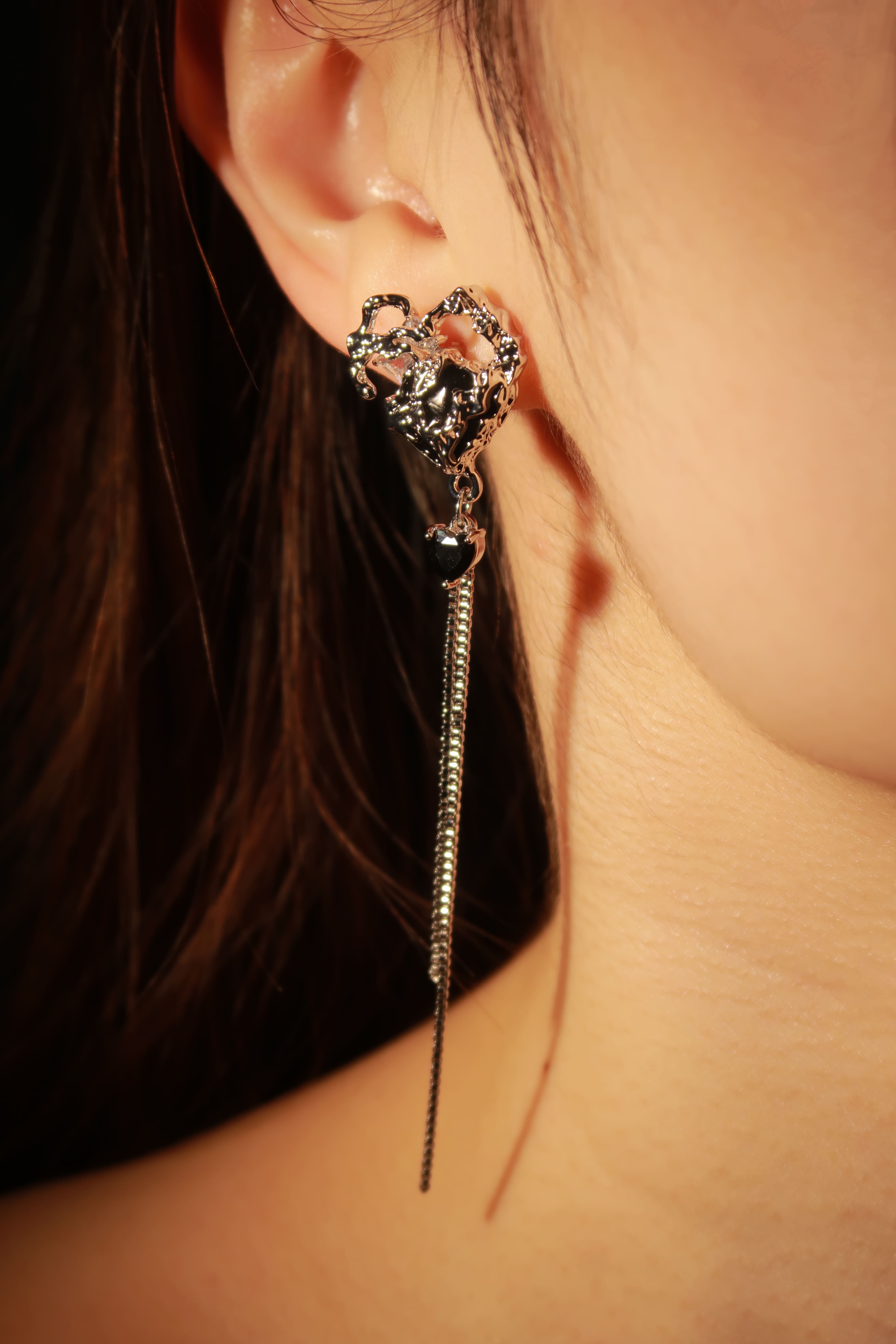 A close-up image of a person wearing a pair of silver-colored bleeding heart earrings.