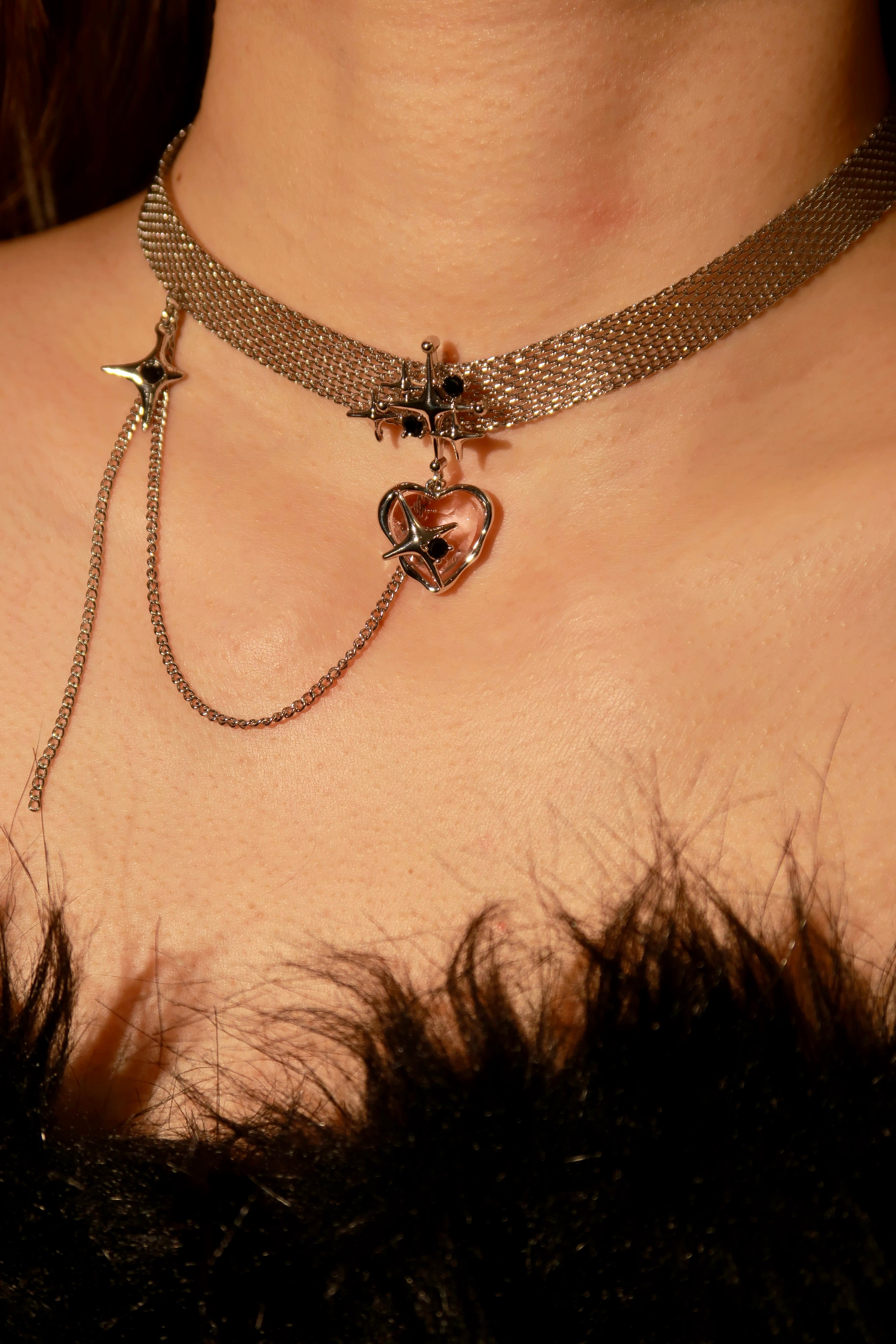 A gold-tone choker necklace with a heart-shaped pendant and a small star charm, worn by a person with visible shoulders and neck.