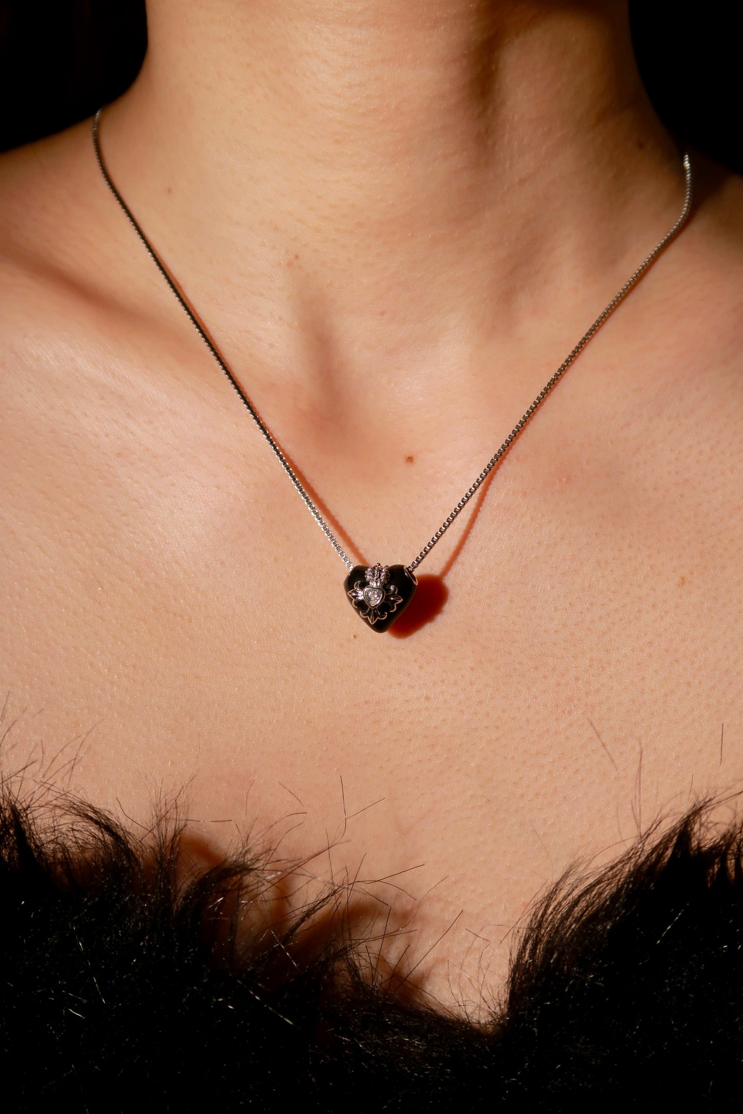Necklace with a heart-shaped pendant on a person's neck against a dark background