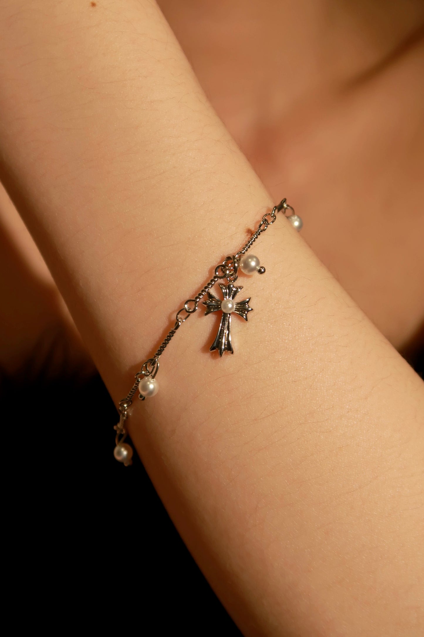 A bracelet with metallic charms, including a cross and a heart, worn on a person's wrist.