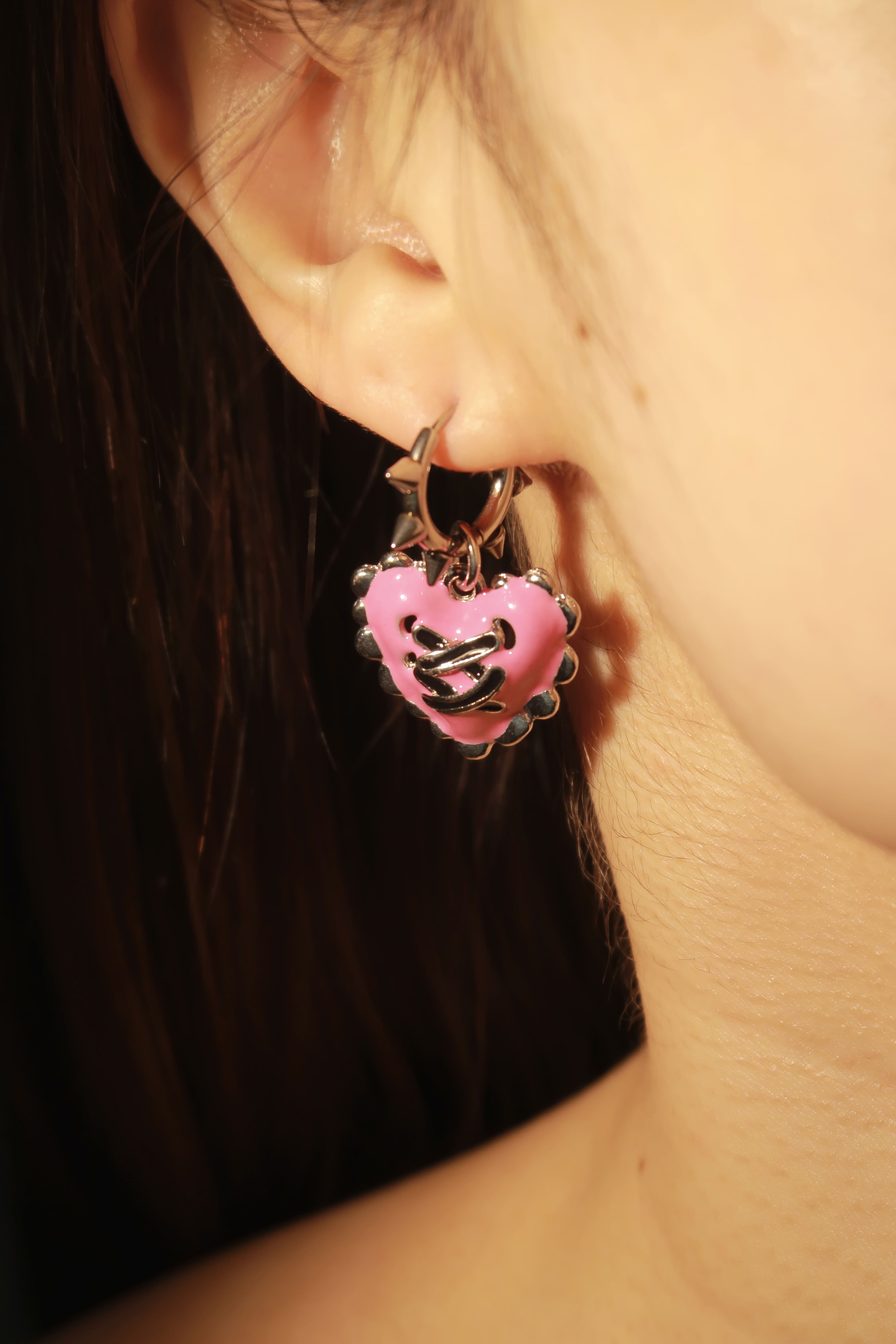 Close-up of an ear wearing a pink heart-shaped earring with a dark background