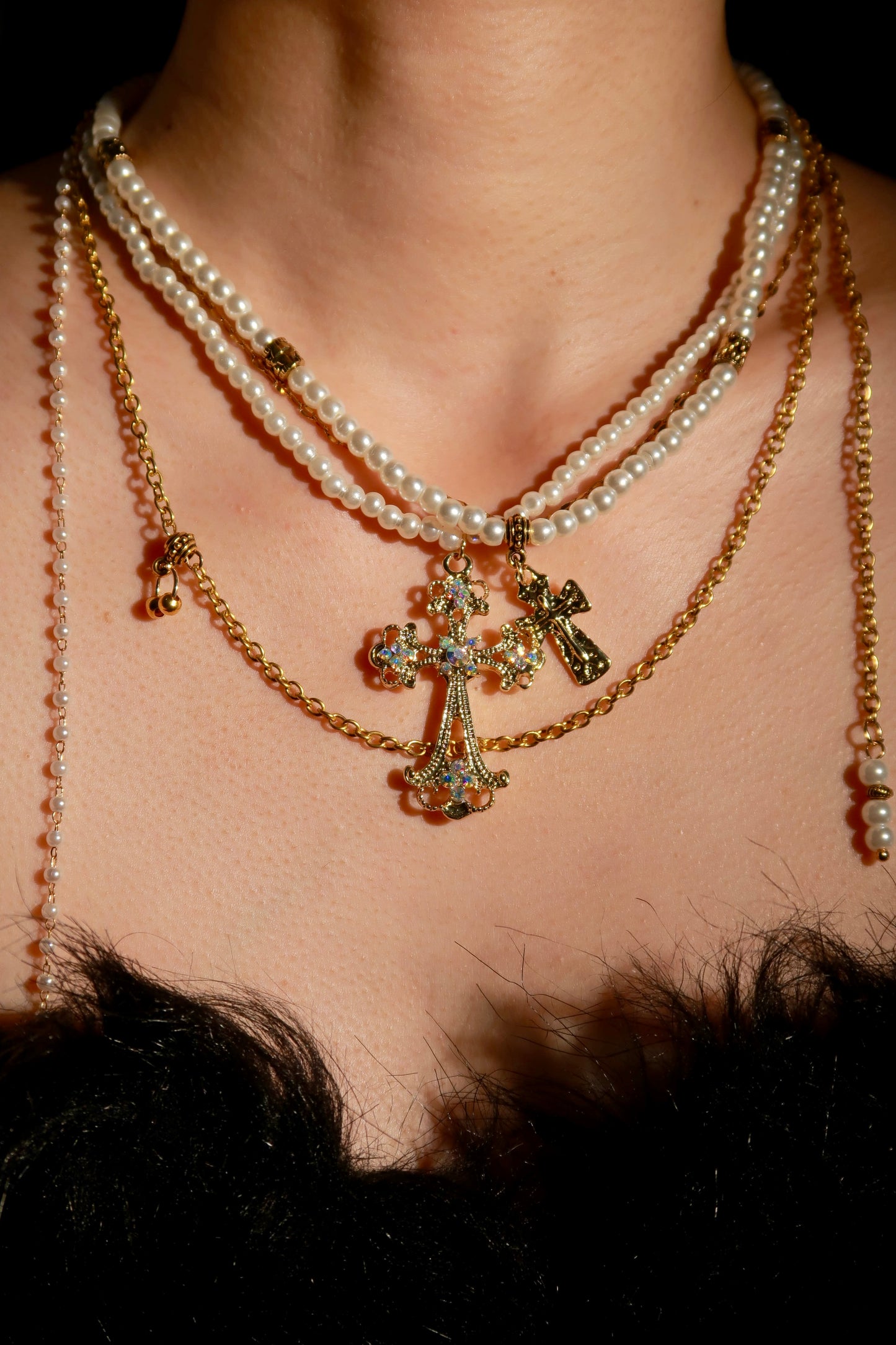 Close-up of a necklace with a cross pendant and pearl strands on a person's neck.