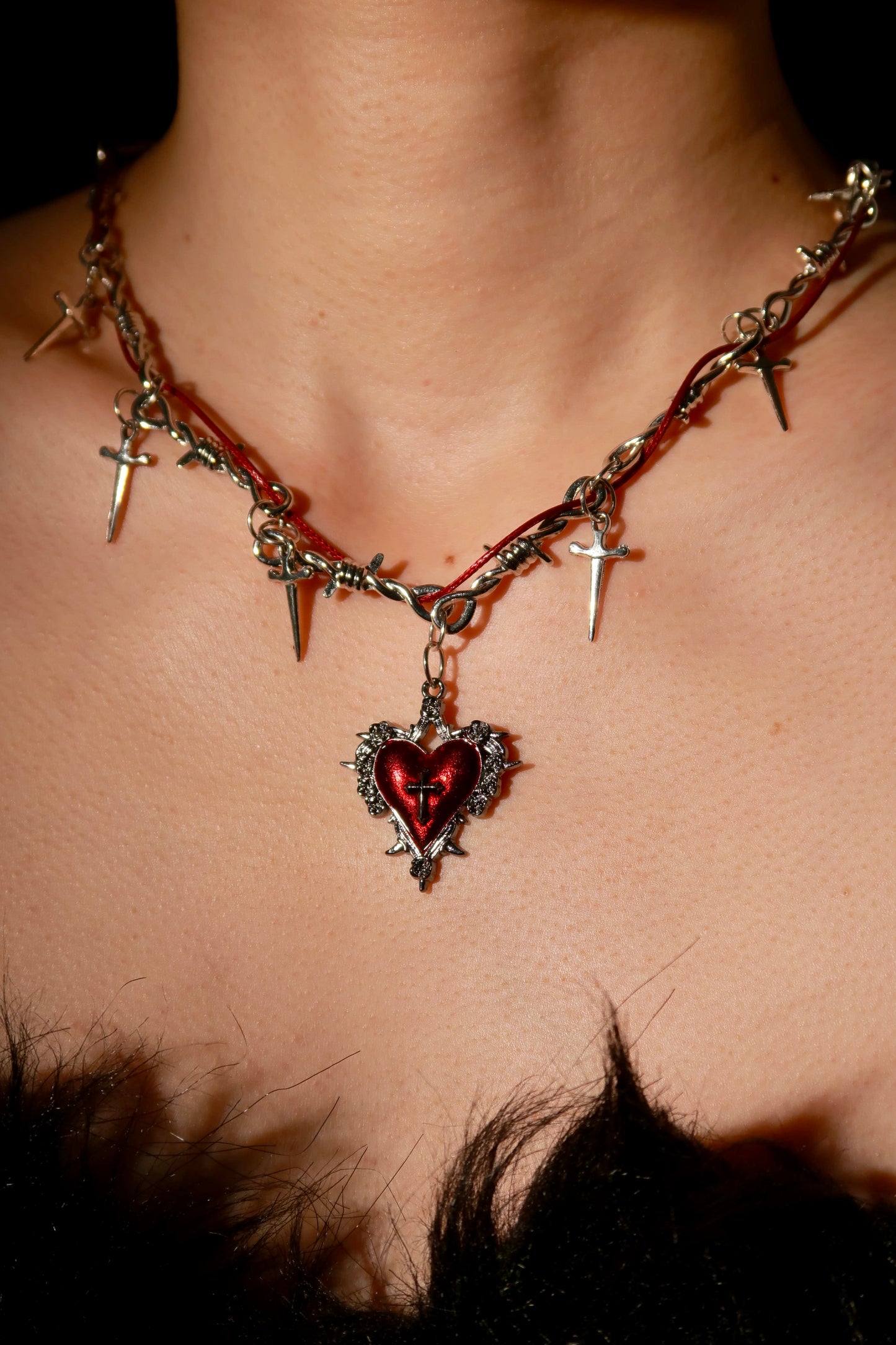 Necklace with heart-shaped pendant and barbed wire design on a person's neck.