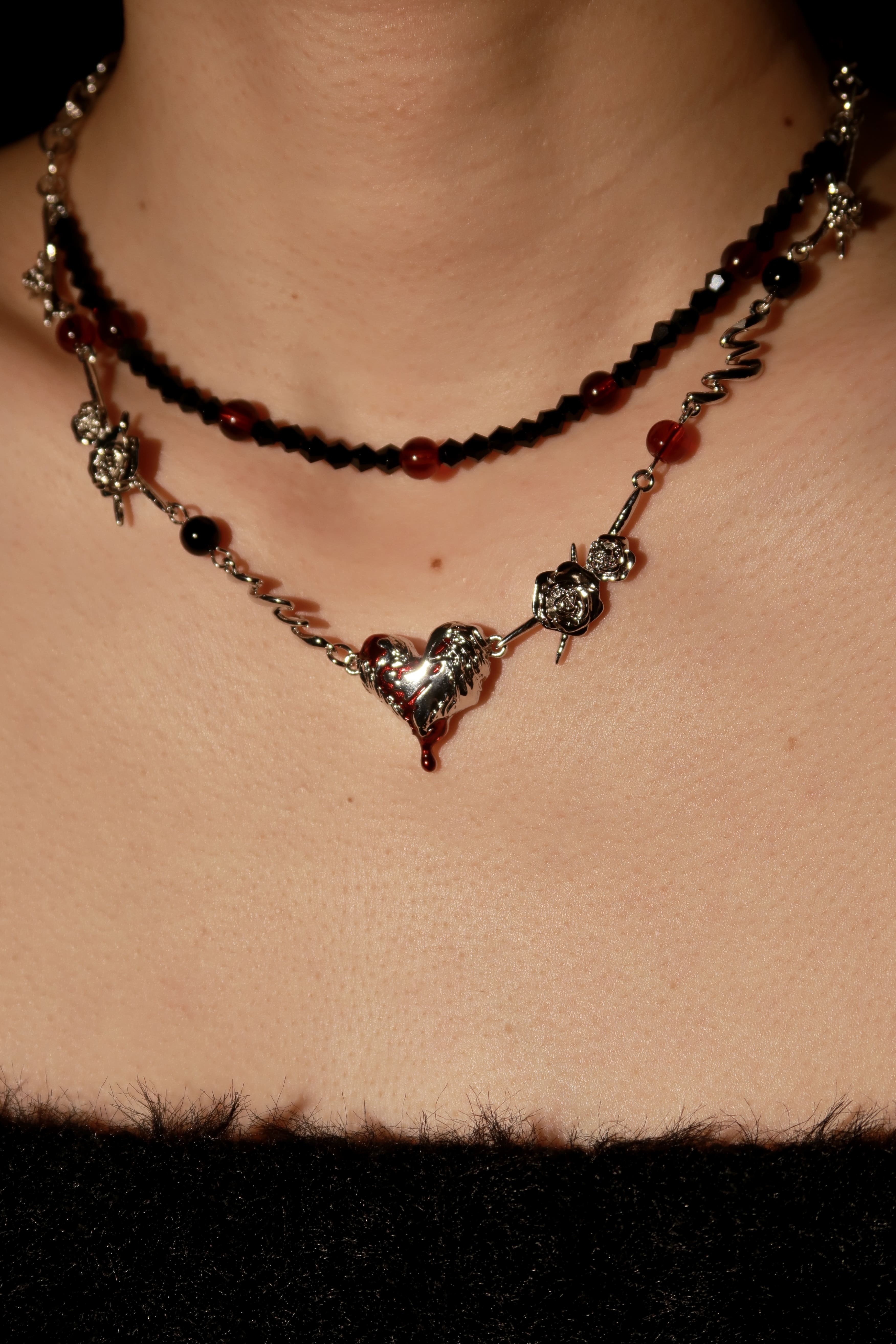 A close-up of a person wearing a multilayered necklace with black beads and heart-shaped pendants, along with other jewelry.
