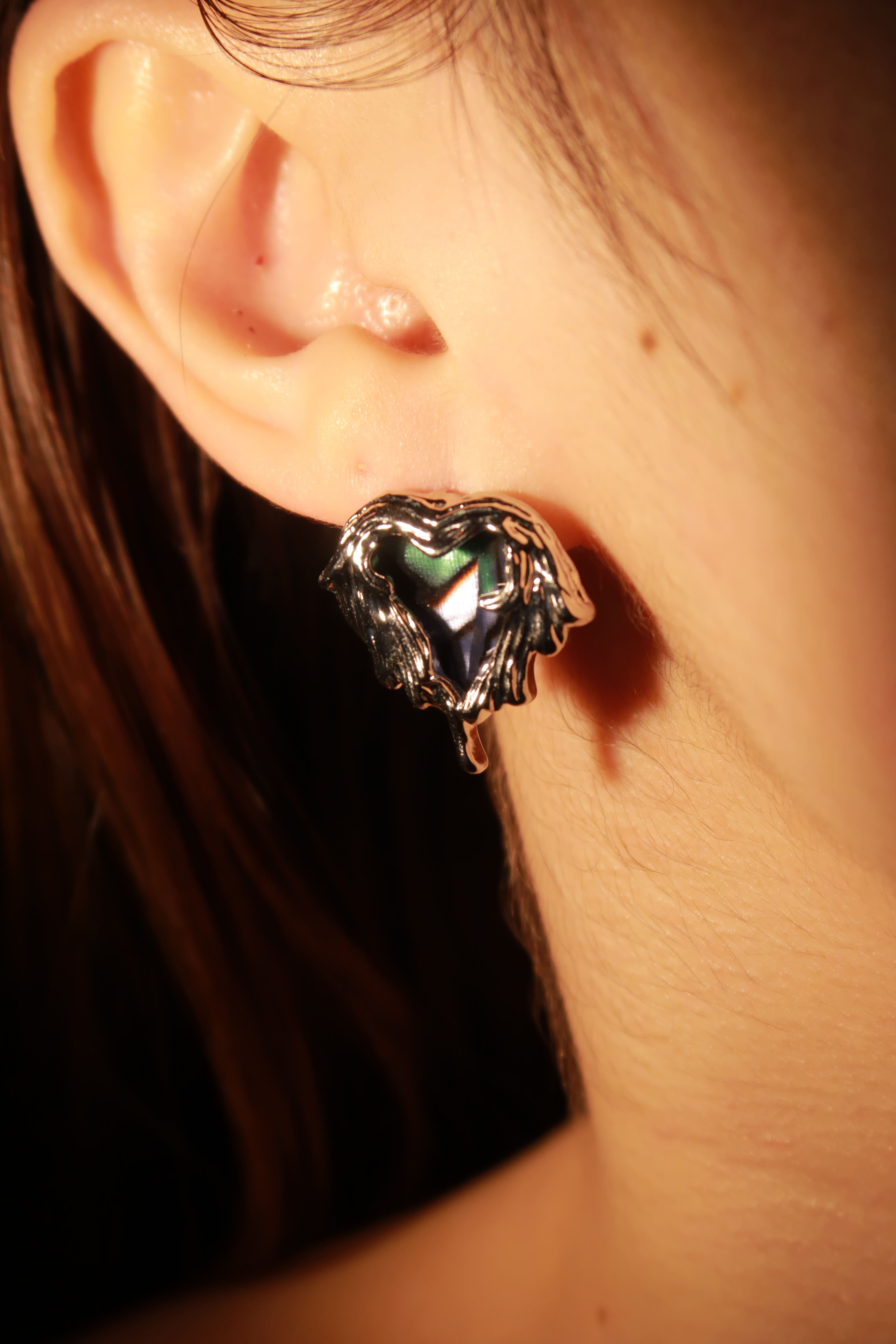 A close-up image of a person wearing a silver-colored hoop earring with a heart-shaped pendant.