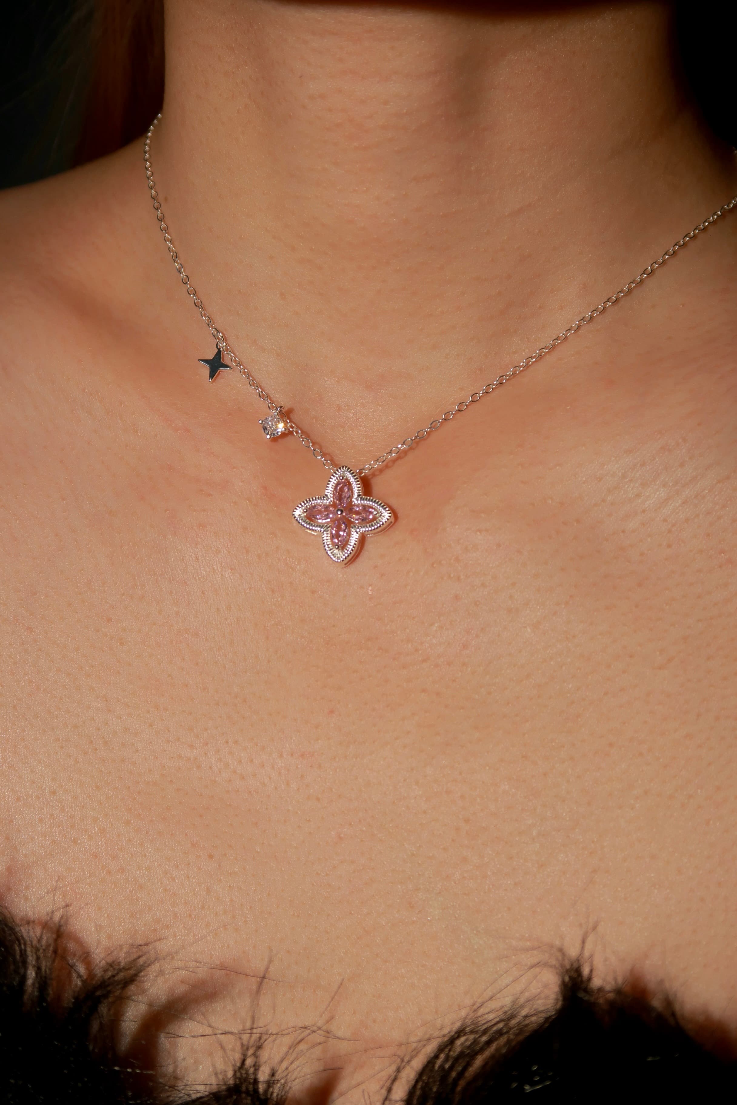 Necklace with a pink clover-shaped pendant on a person's neck