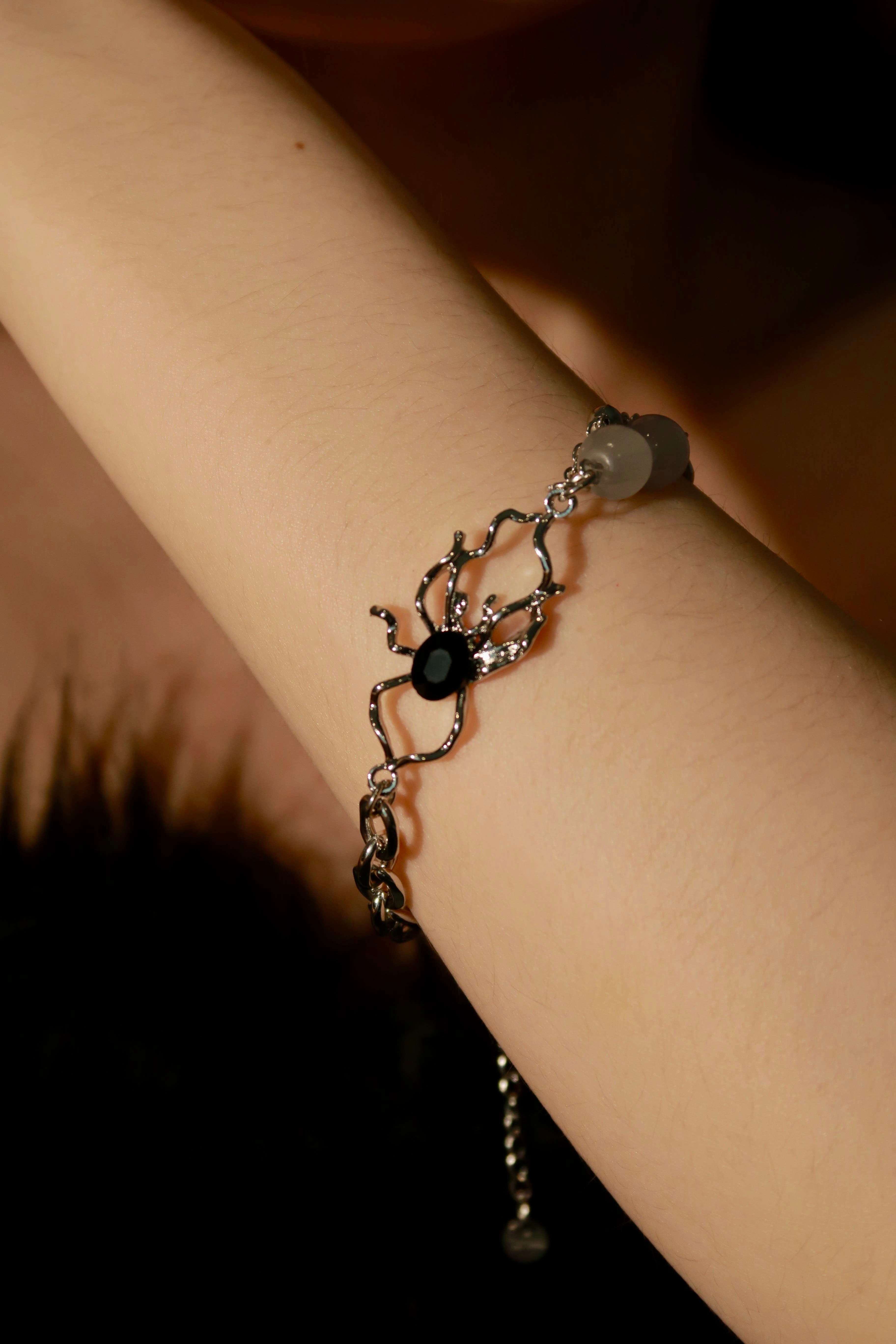 A close-up image of a silver bracelet with a tangled spider design, being worn on a person's wrist.