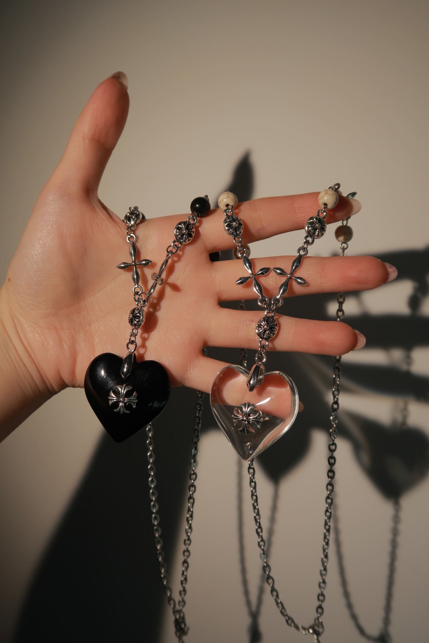 Hand holding multiple necklaces with various pendants against a neutral background