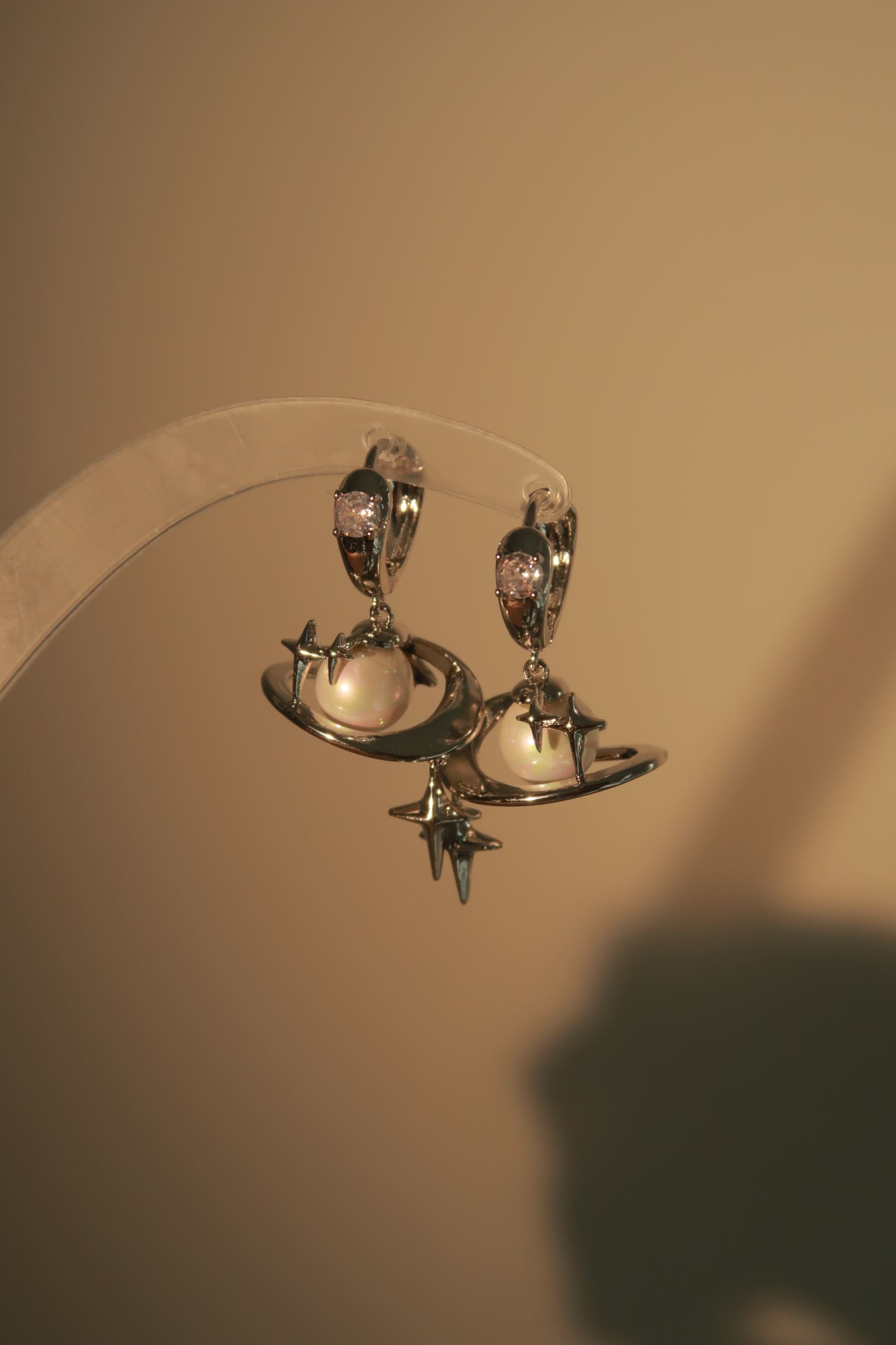 A pair of silver-colored planet-themed earrings displayed against a beige background.