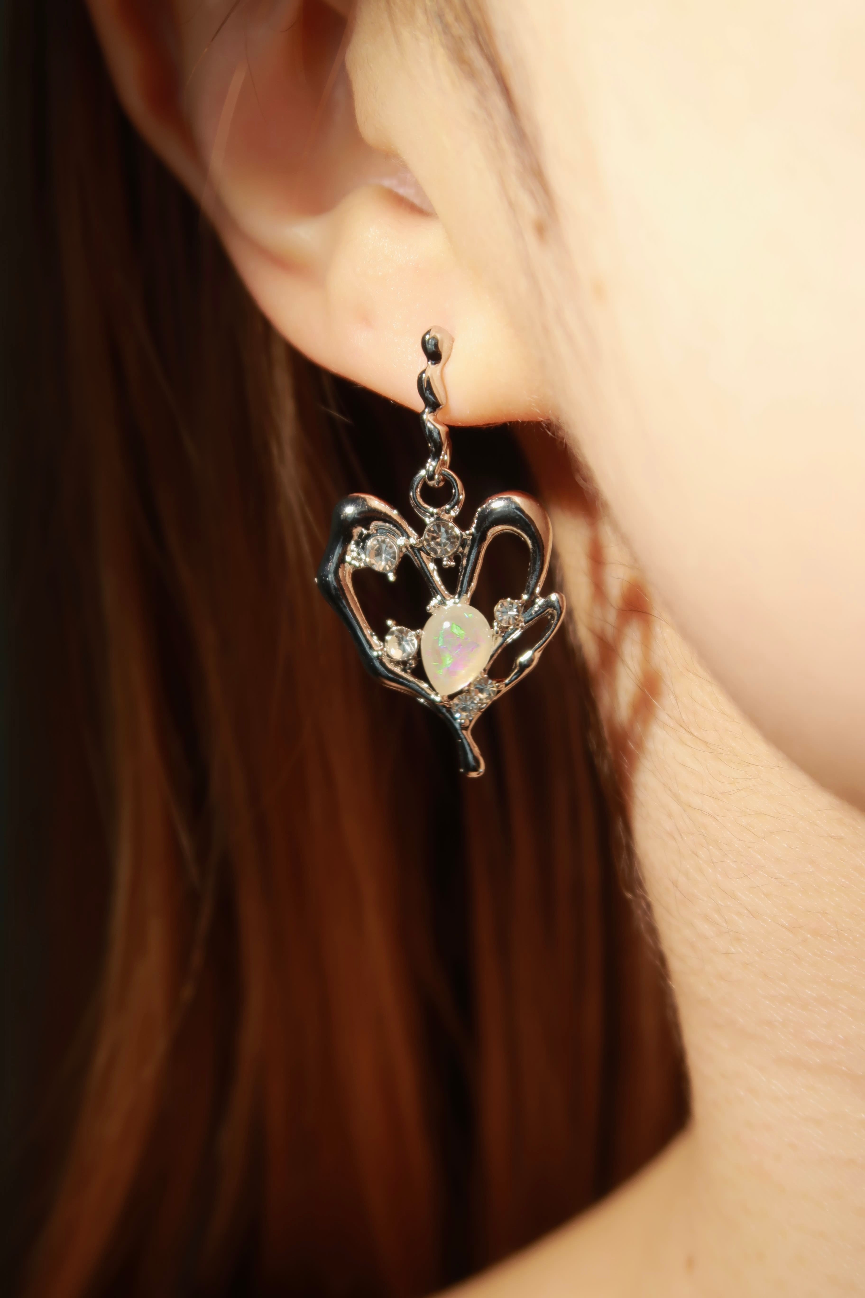 Heart-shaped earring with opal stone worn by a person