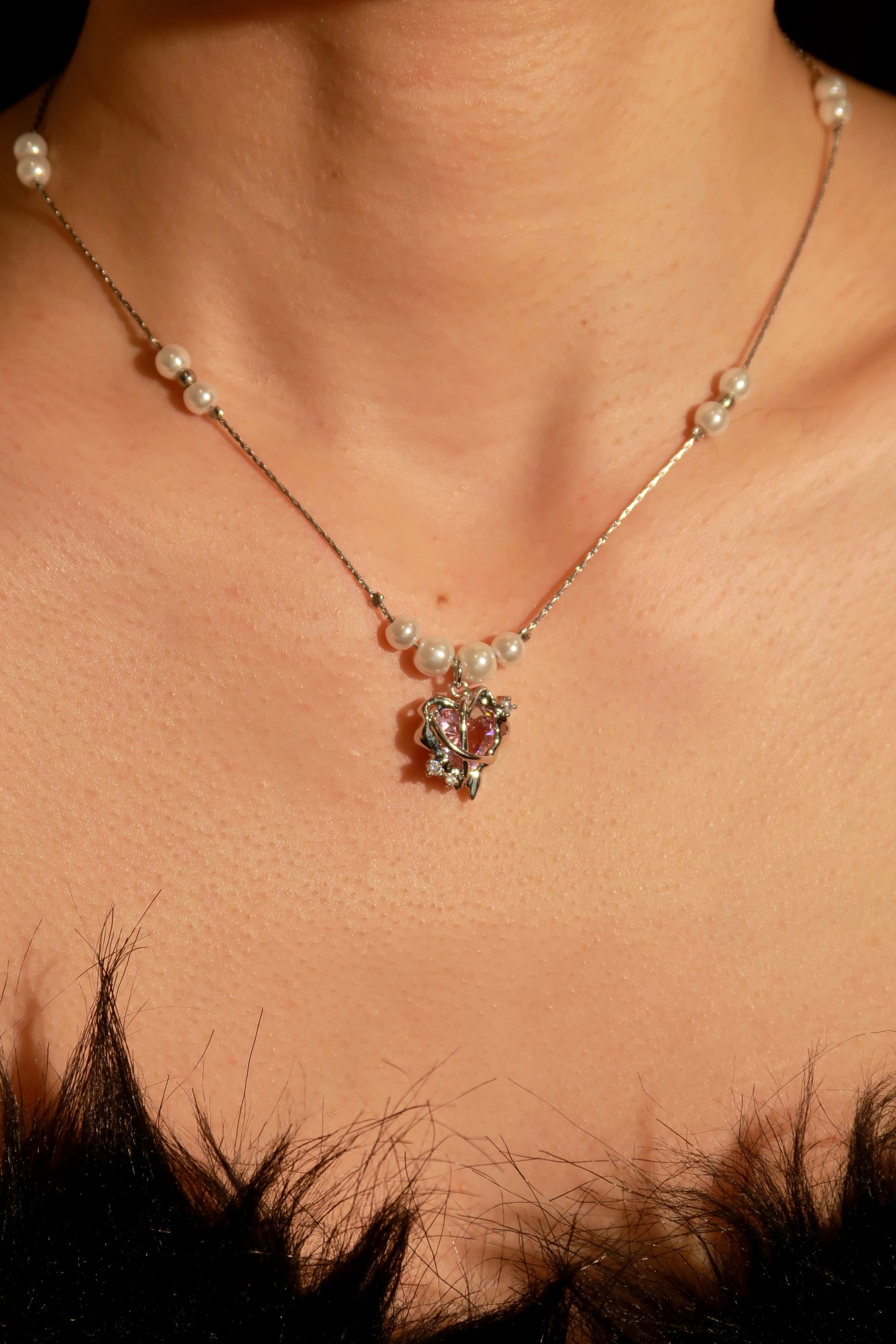 A silver-colored necklace with a floral pendant and pearl-like embellishments, worn by a person with a feathered garment in the background.