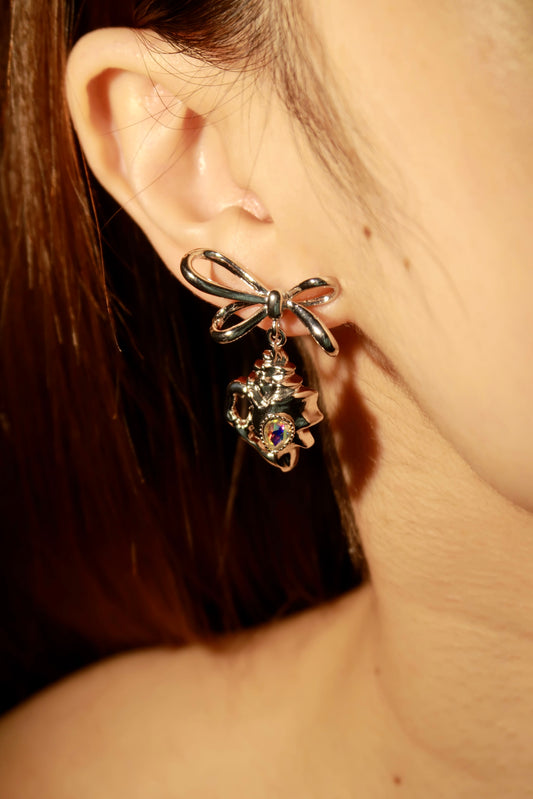 Close-up of a silver bow-shaped earring with a gemstone on an ear.