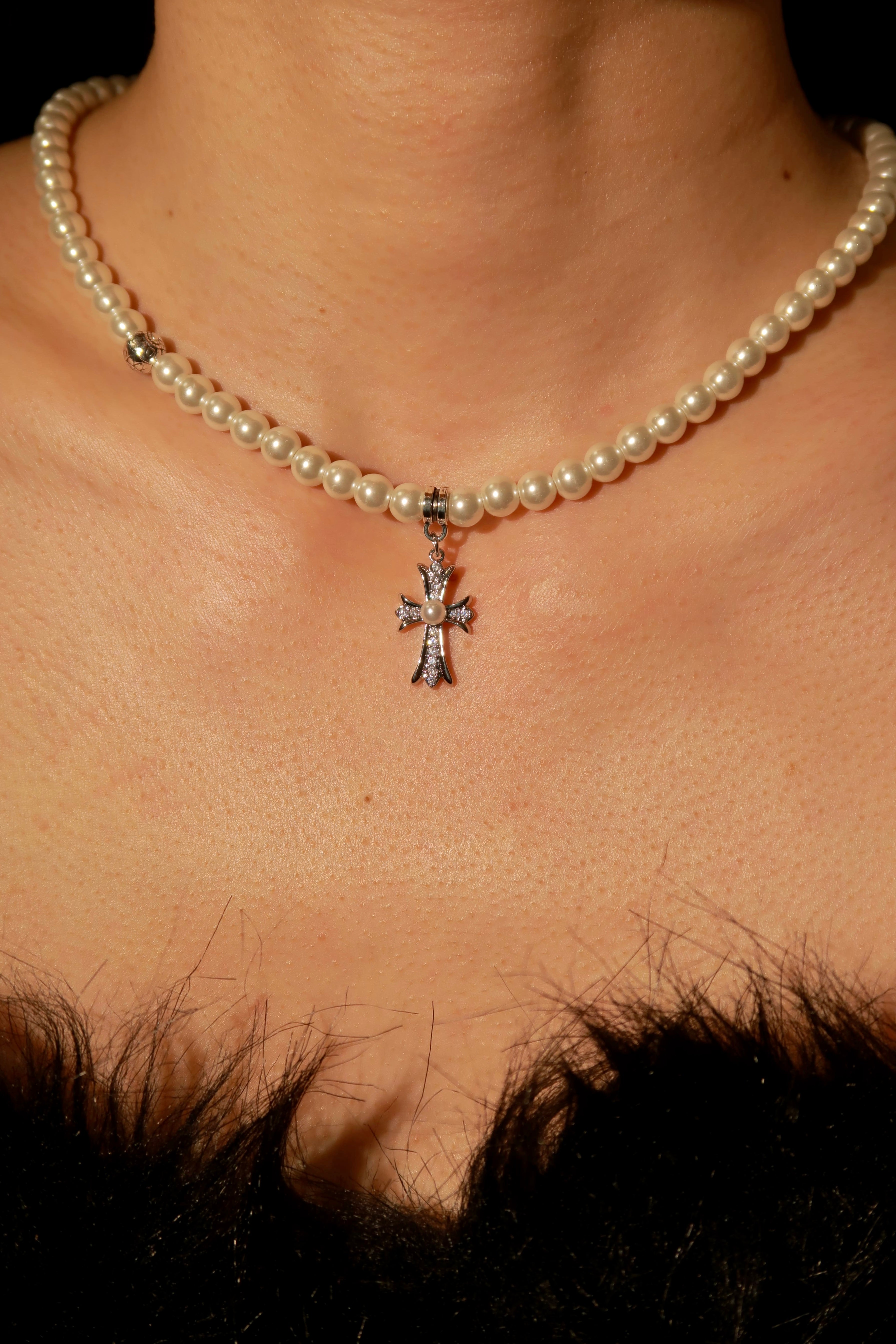 A close-up image of a person wearing a pearl necklace with a silver cross pendant.