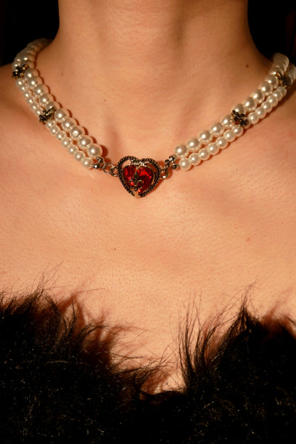 Pearl necklace with a heart-shaped red gemstone on a person wearing fur.