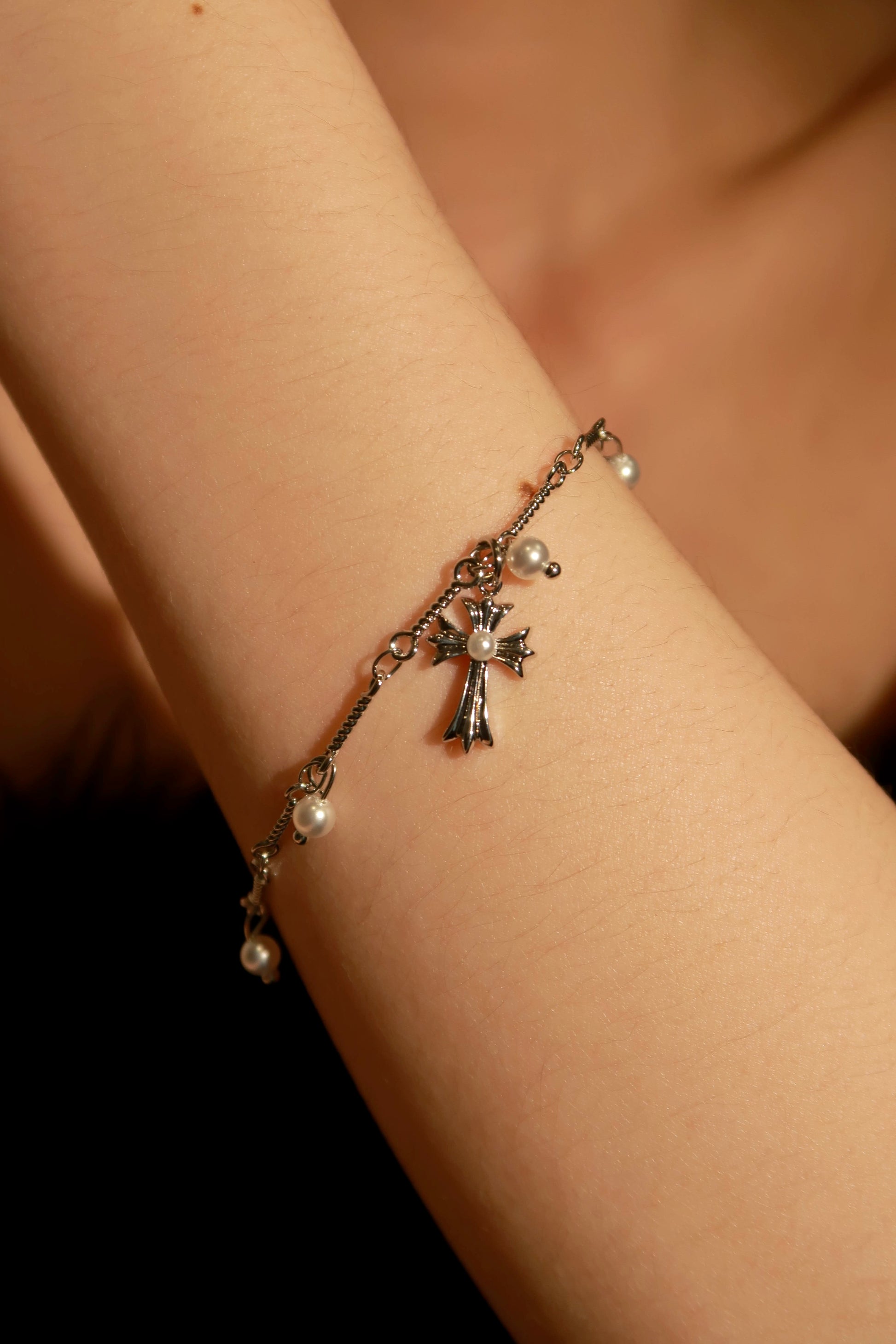 A bracelet with metallic charms, including a cross and a heart, worn on a person's wrist.