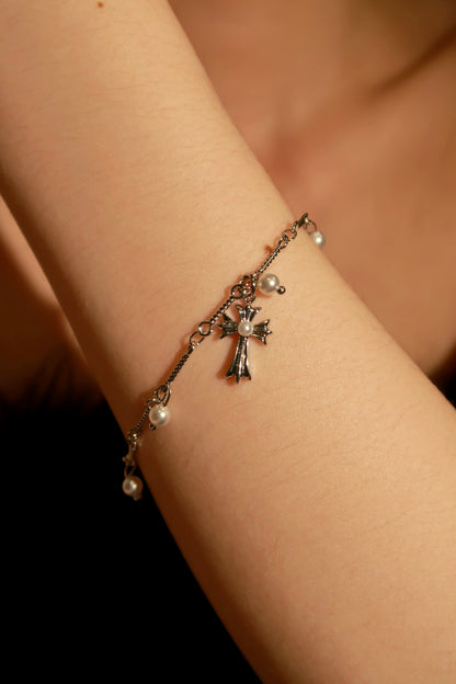 A bracelet with metallic charms, including a cross and a heart, worn on a person's wrist.