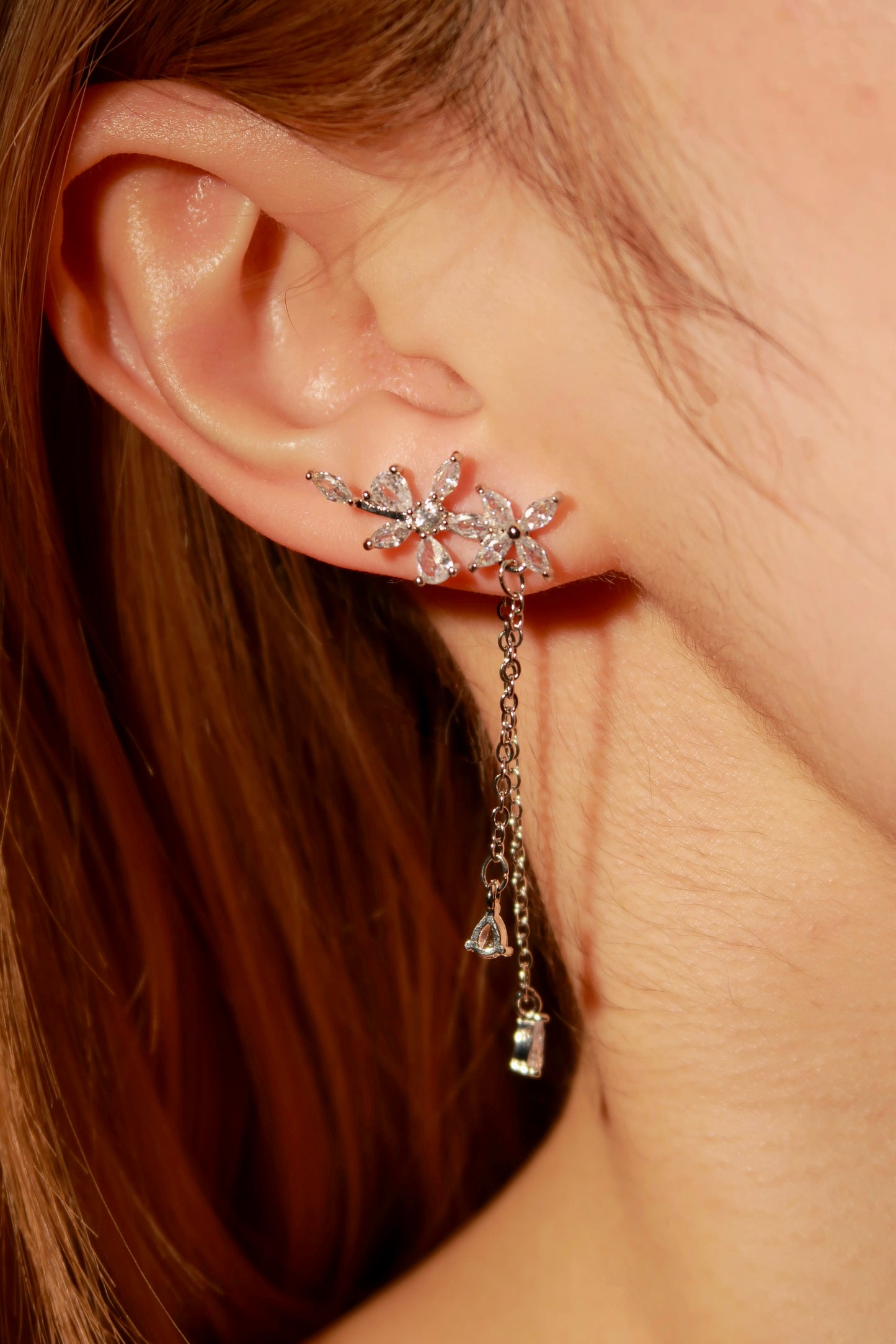 Close-up of a person wearing a floral earring with dangling crystals.