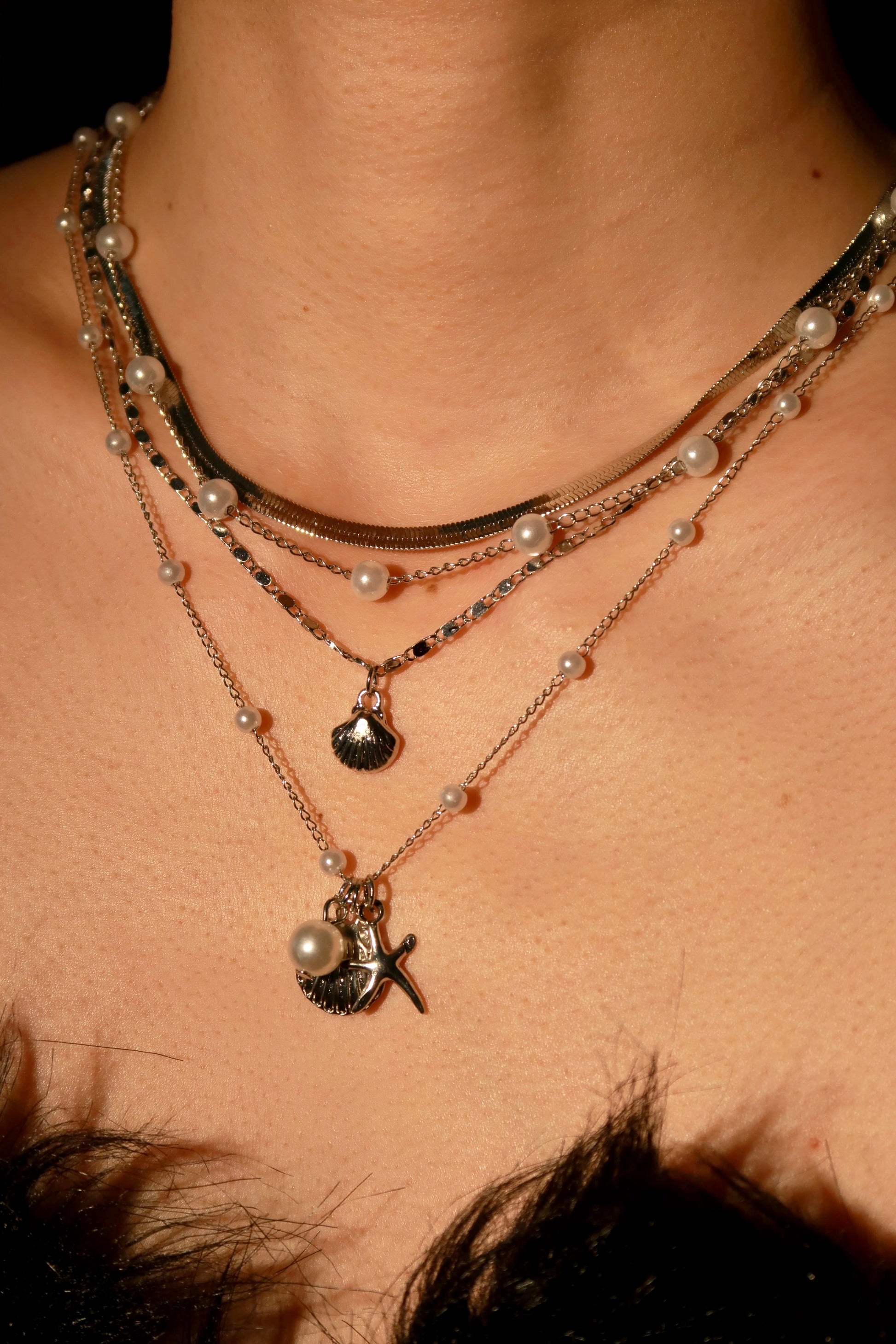 Close-up of layered necklaces with pearls and charms on a person's neck.