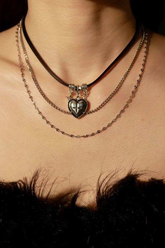 Close-up of a person wearing multiple necklaces with a heart pendant on a dark background