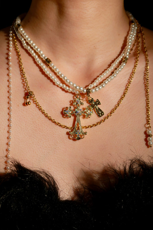 Close-up of a necklace with a cross pendant and pearl strands on a person's neck.