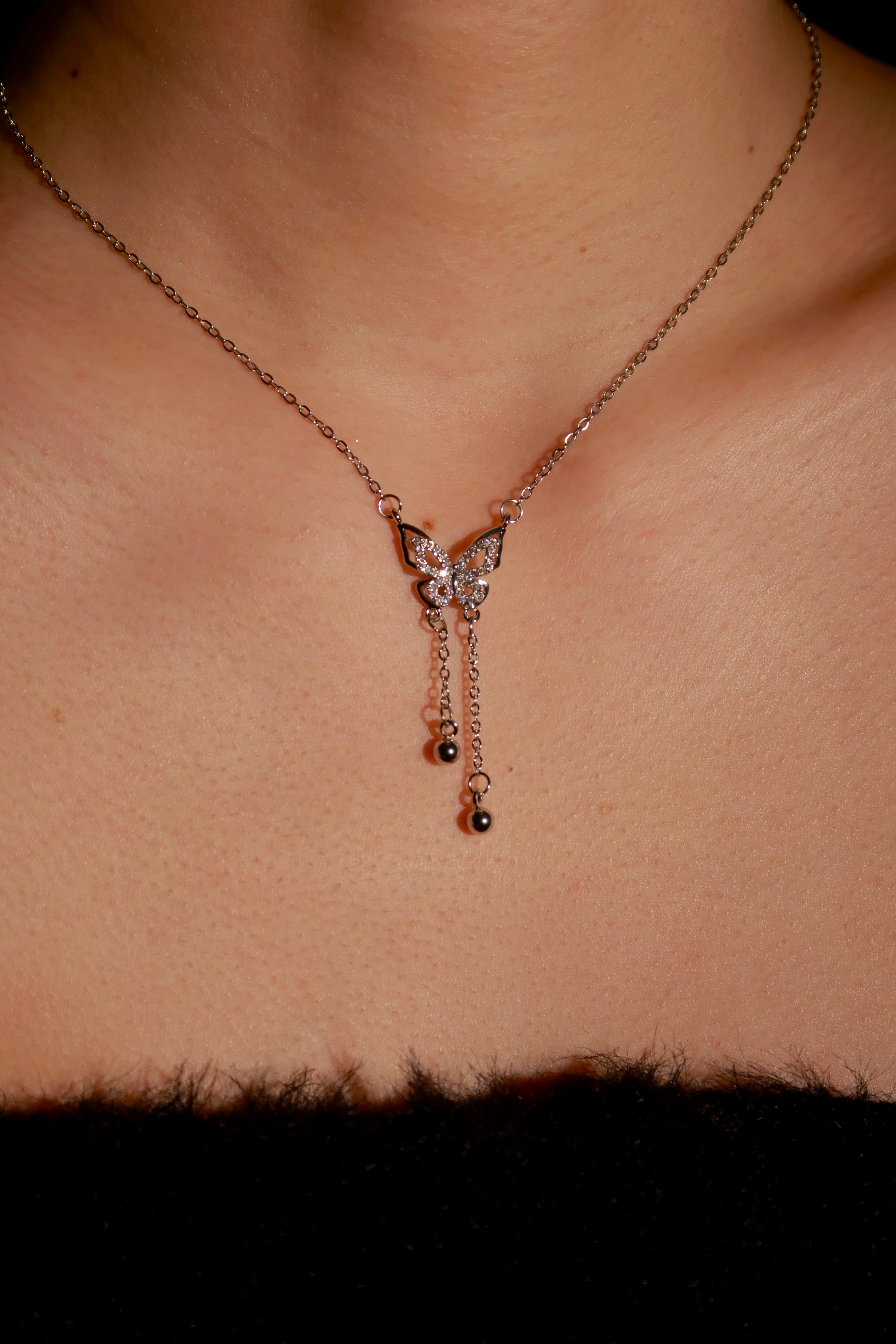 A silver-colored butterfly necklace with a small pearl drop, worn by a person with a visible collarbone and clavicle.