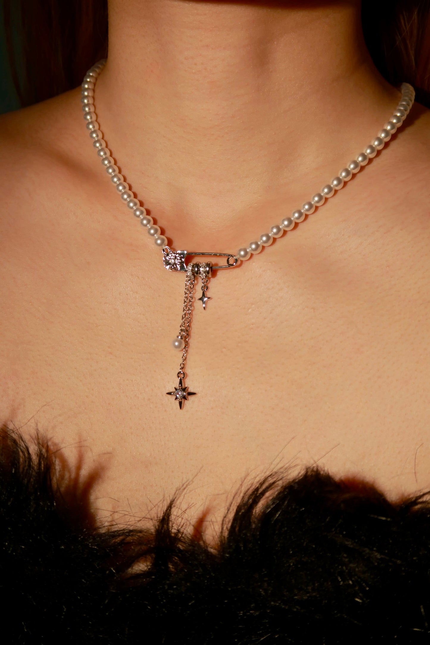 Pearl necklace with star pendant on a person wearing a black feathered garment.