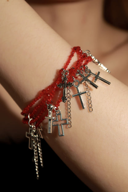 Red beaded bracelet with silver cross charms on a wrist against a blurred background