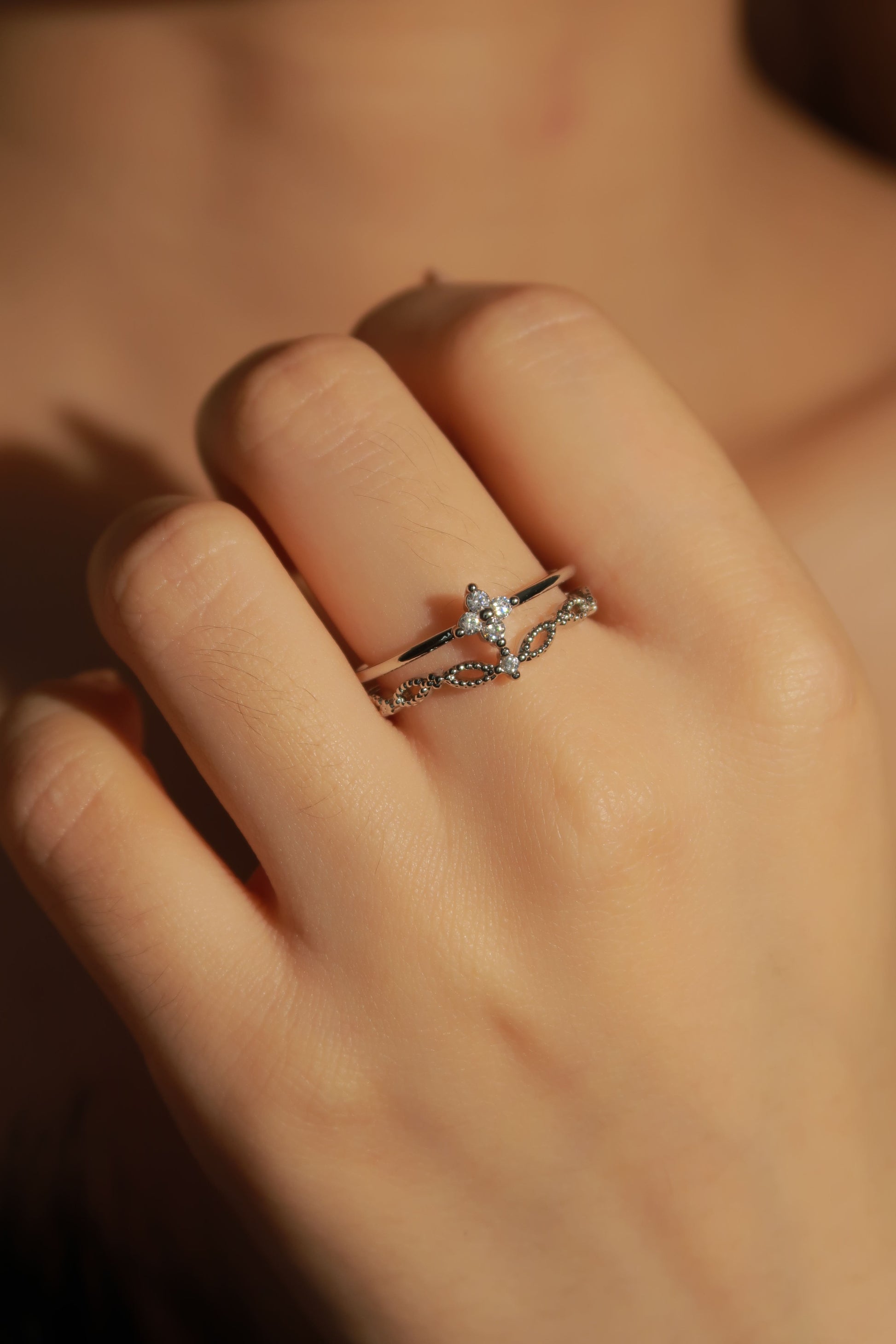Close-up of a hand wearing a silver ring with a diamond on a blurred background
