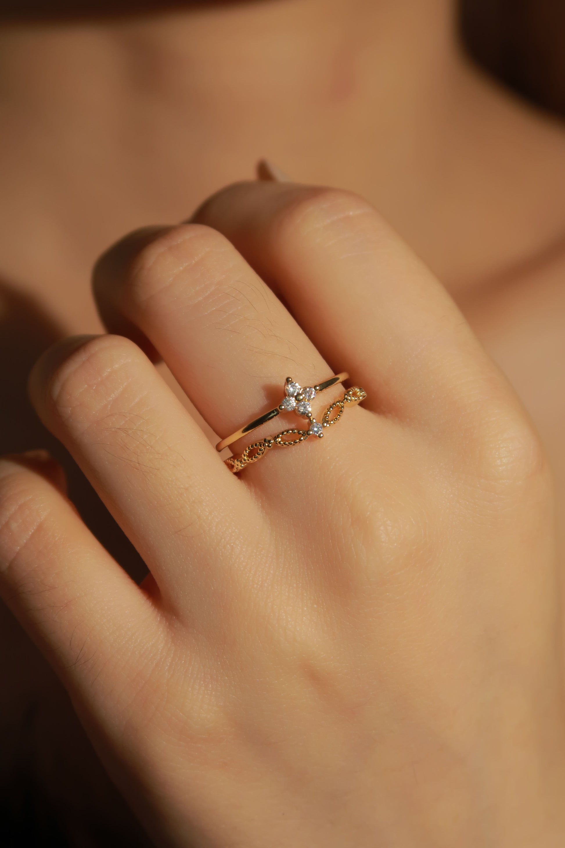 Close-up of a hand wearing two gold rings with star designs on a blurred background