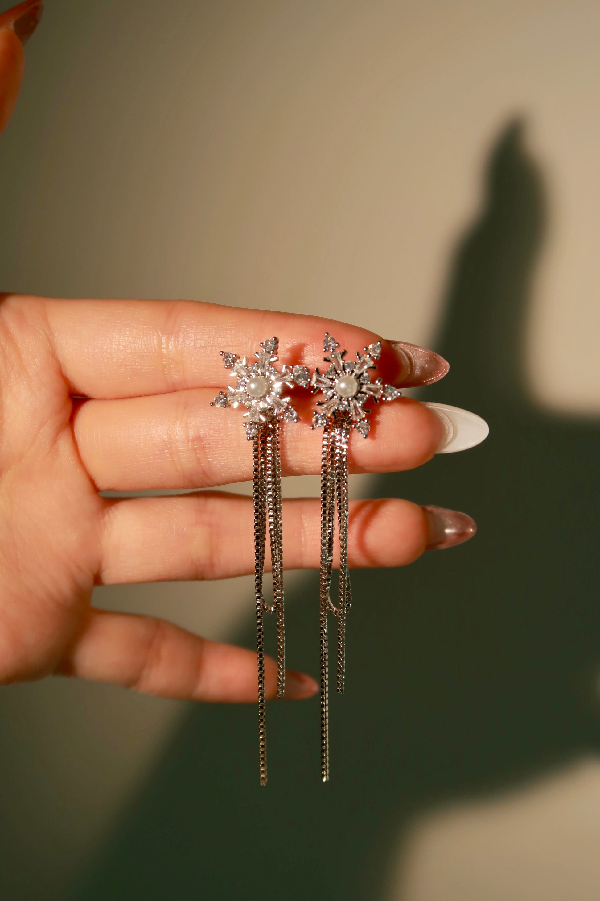 Hand holding a pair of star-shaped earrings with dangling chains against a neutral background