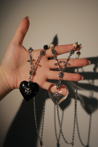 Hand holding multiple necklaces with various pendants against a neutral background