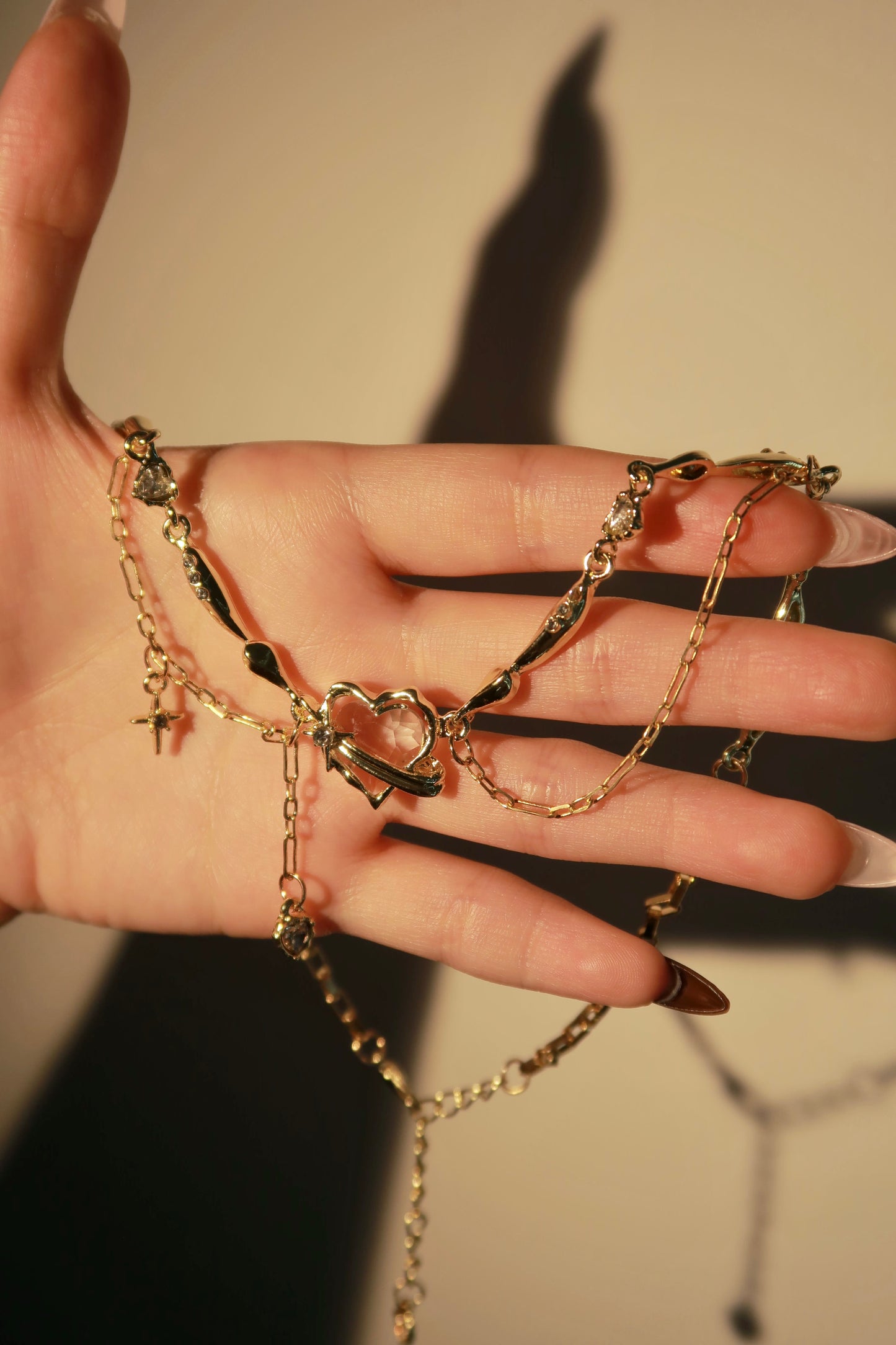 Hand wearing multiple gold chains with a neutral background