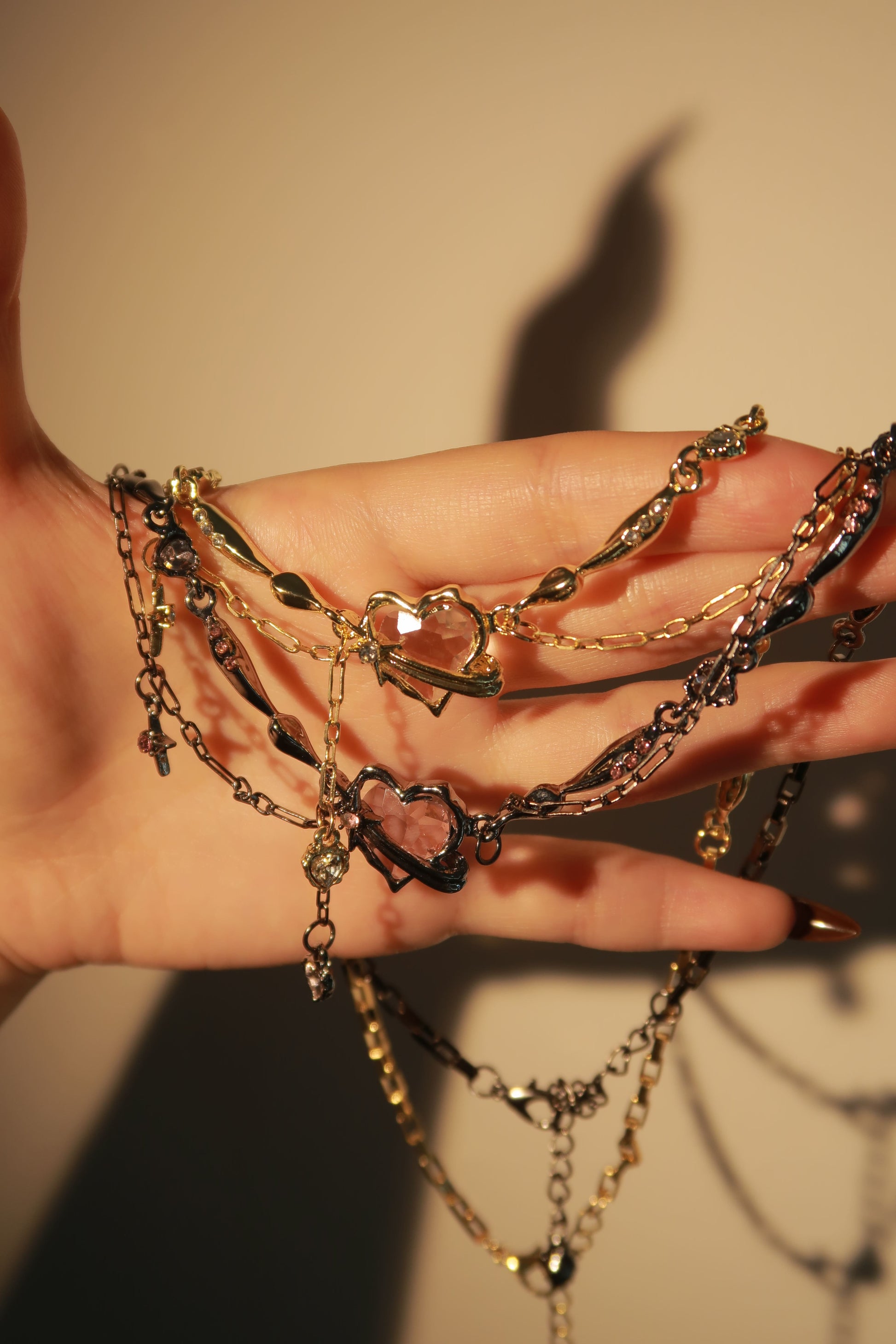 Hand wearing multiple gold and black chain bracelets on a neutral background