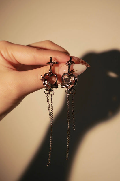 Hand holding a pair of gold earrings with chain details against a beige background