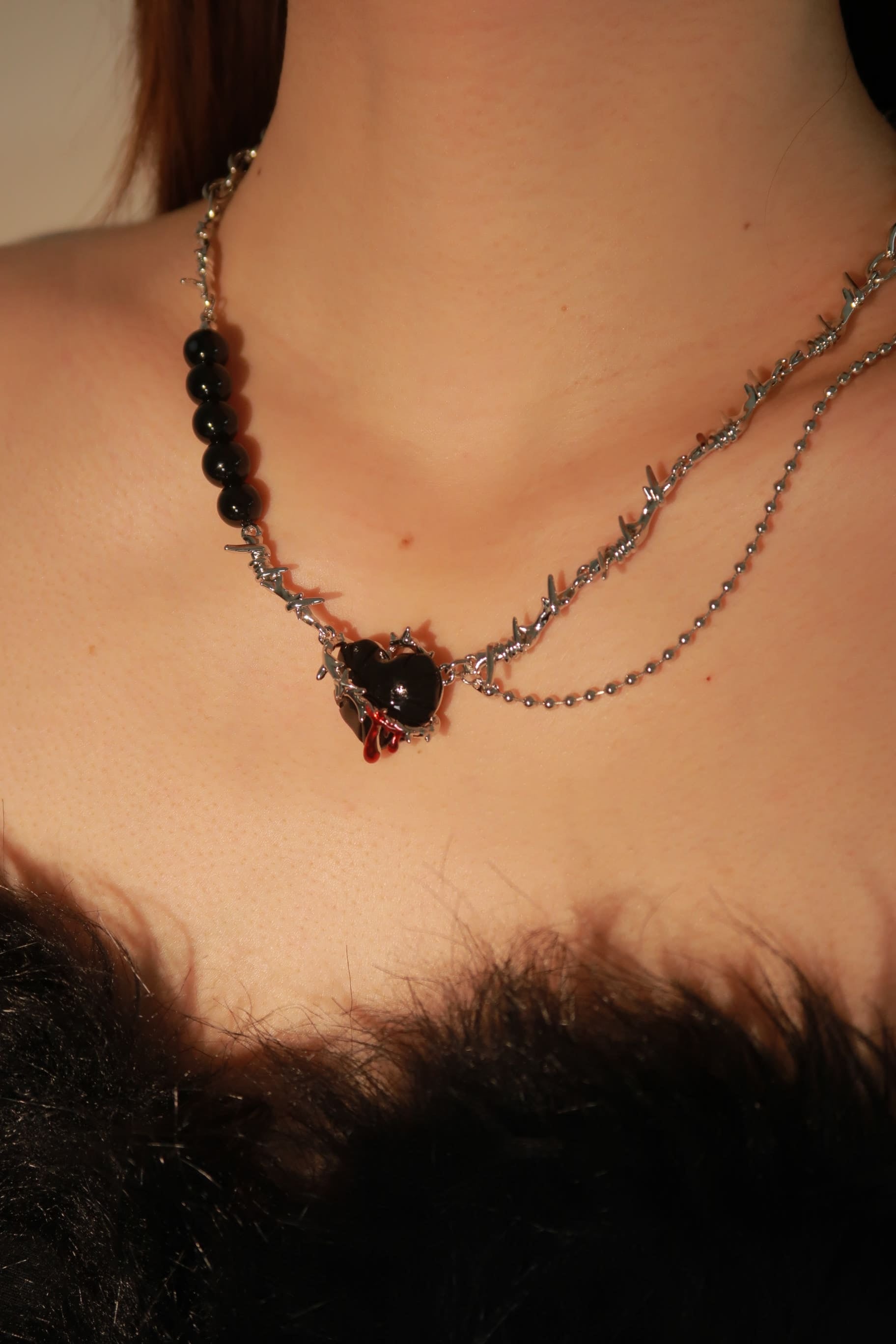 A close-up image of a person wearing a black beaded necklace with a heart-shaped pendant, part of the 'gothic romance' style.