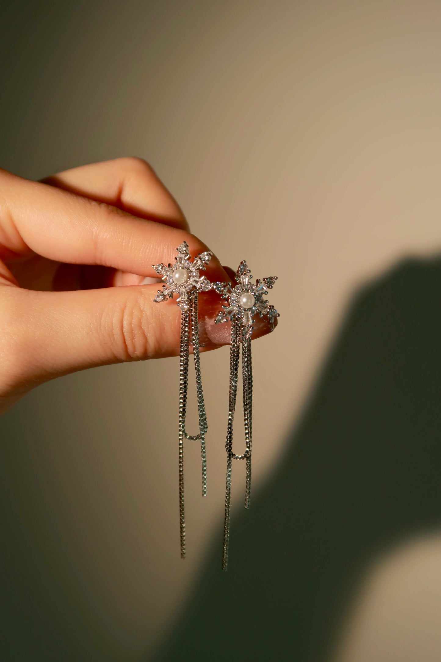 Silver snowflake earrings held by a hand against a neutral background