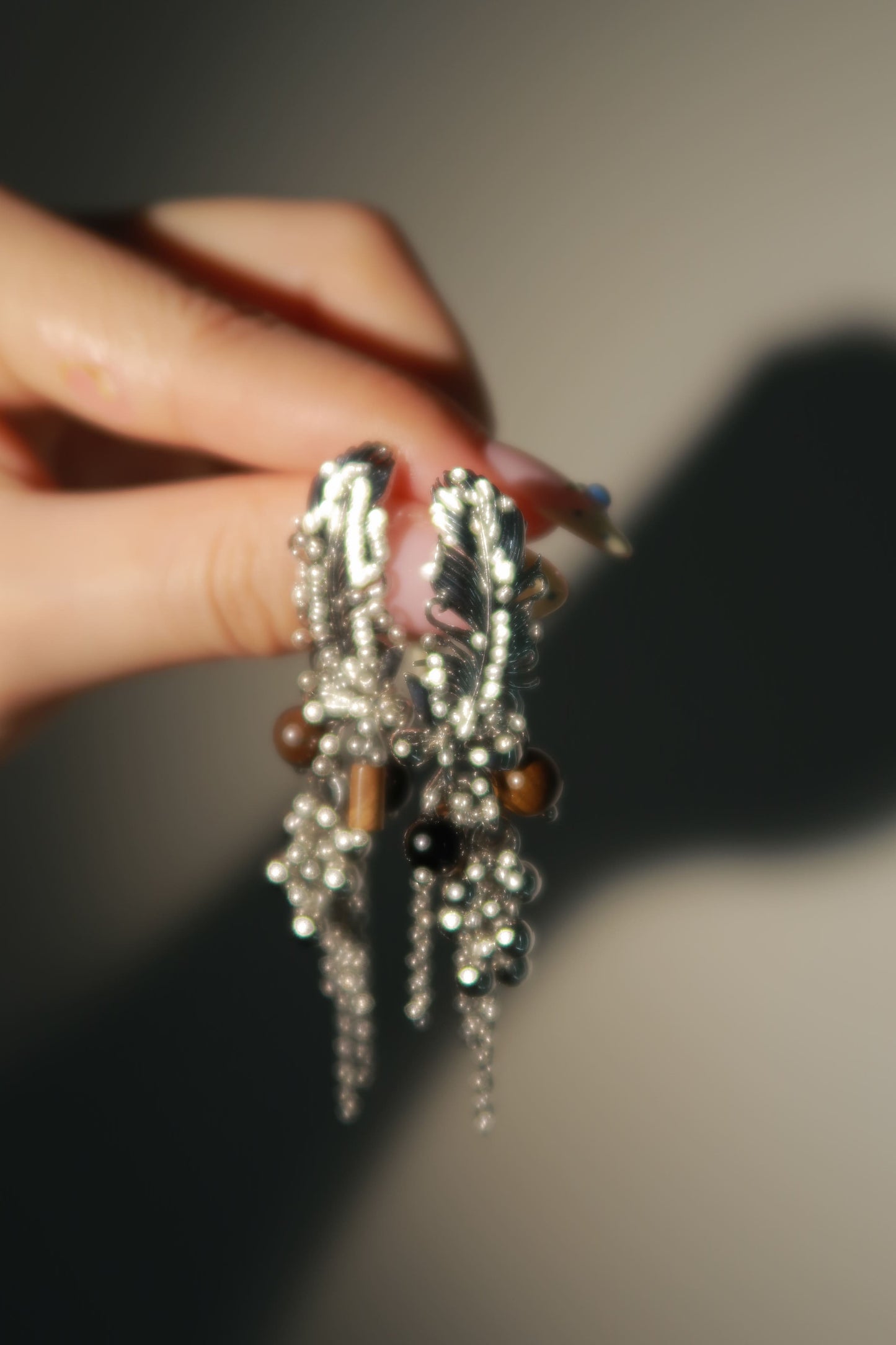 Close-up of a hand holding a decorative hair clip with beads and feathers against a neutral background
