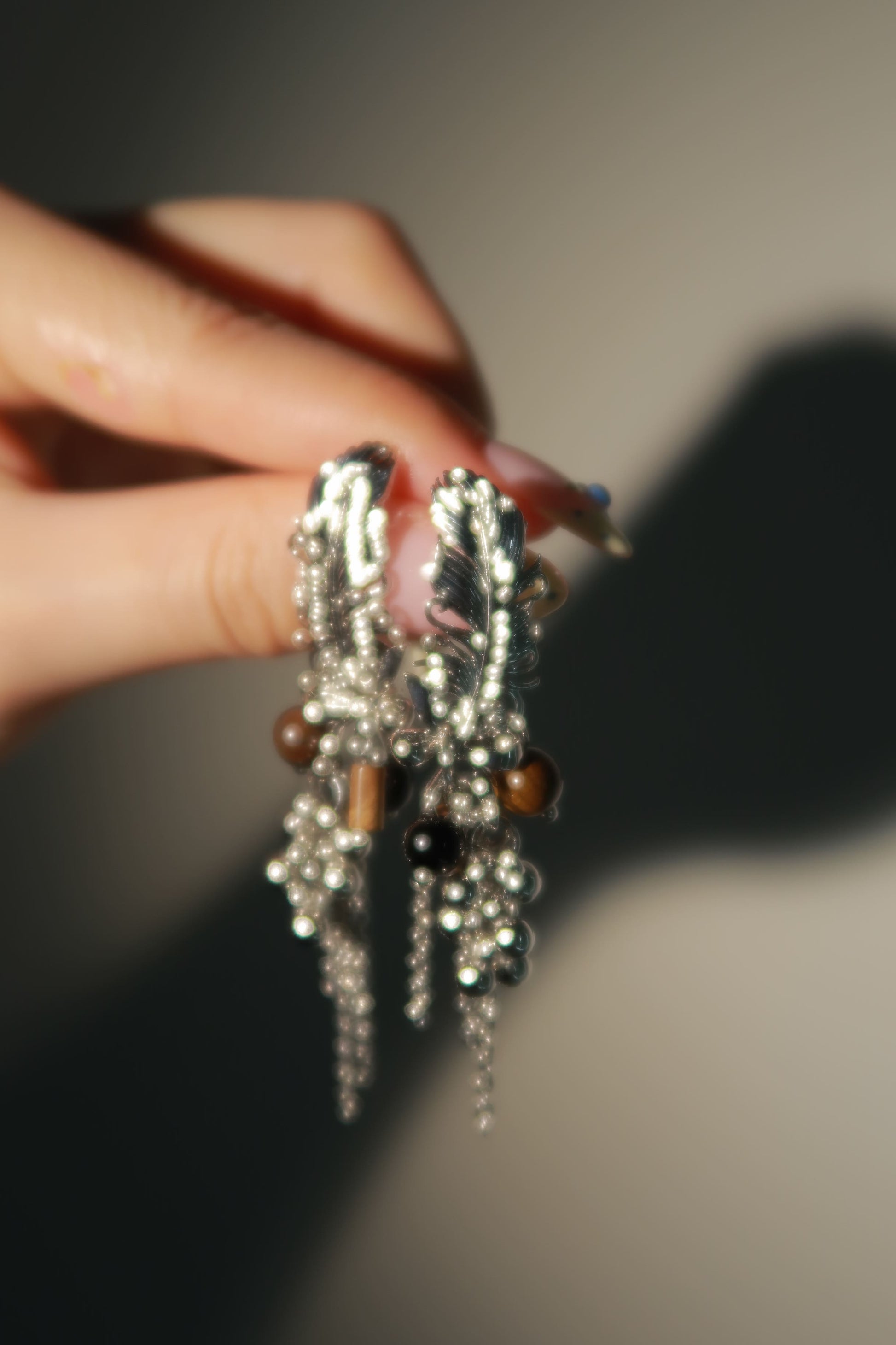 Close-up of a hand holding a decorative hair clip with beads and feathers against a neutral background